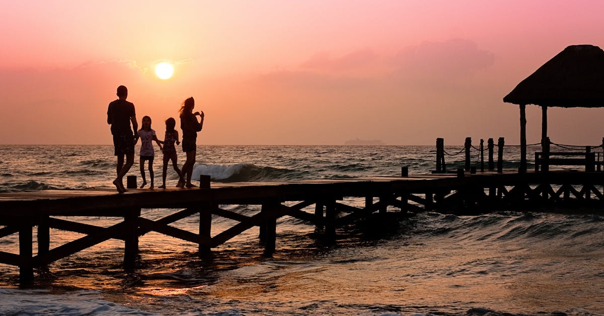 Silhouetted family enjoys a stroll on the beach pier at a vibrant sunset over the ocean waves.